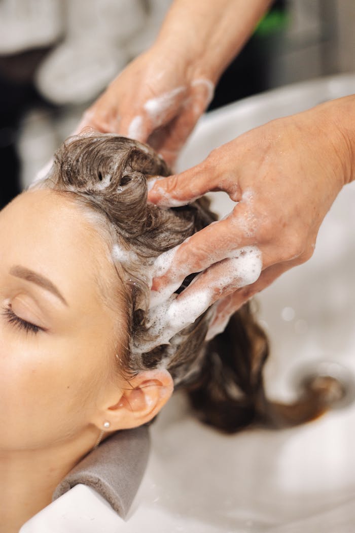 Woman enjoying a calming hair wash with foam and massage at a beauty salon.