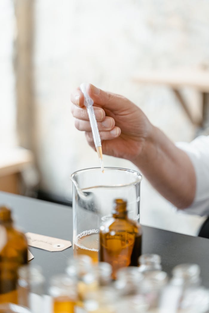 Close-up of a hand using a dropper to add liquid to a glass beaker in apothecary setting.